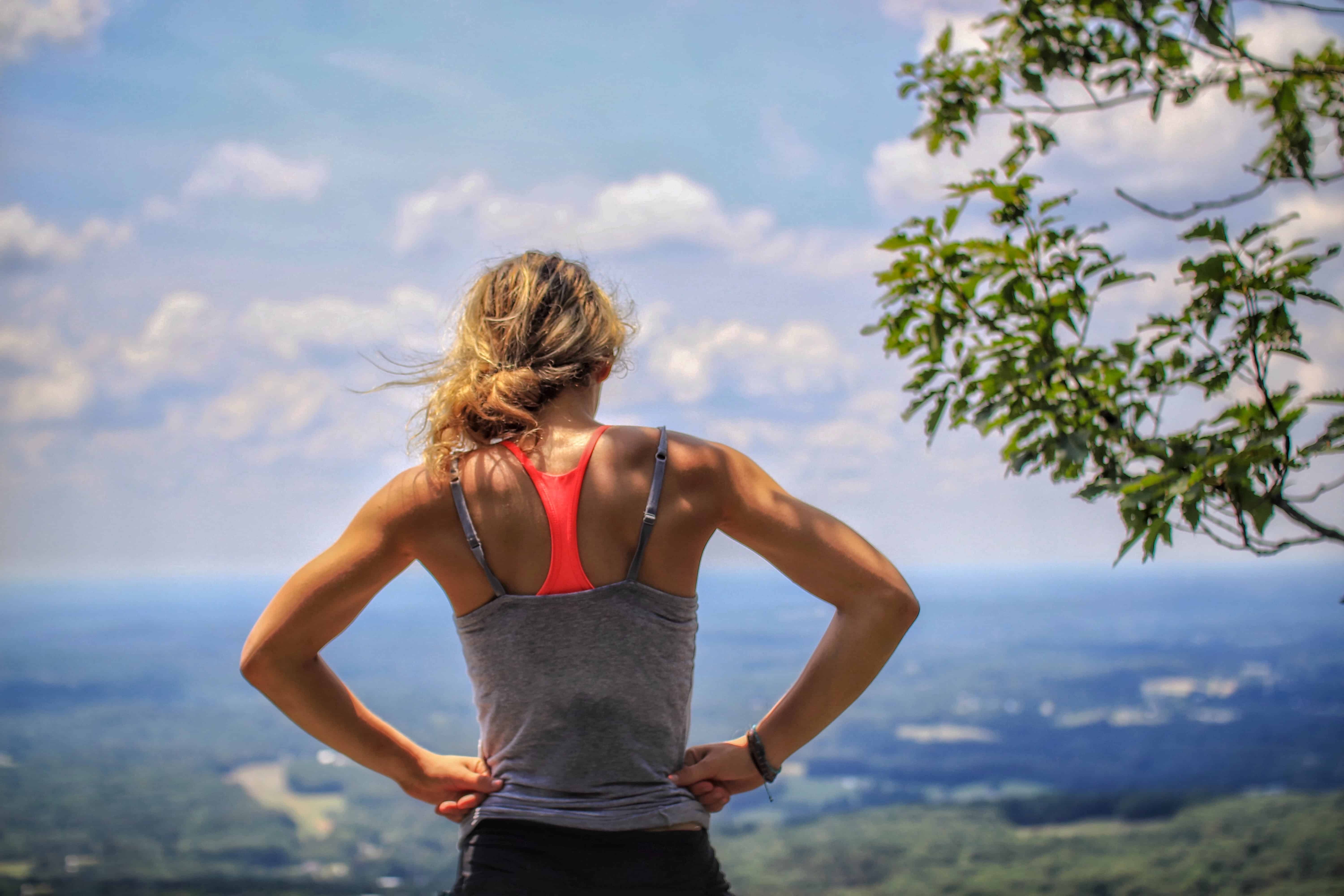 Drive Sports Medicine. Woman standing with hands on her hips on top of a mountain looking out over the view in the sunshine