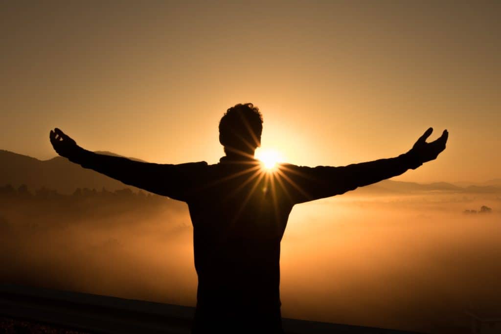 Man standing with arms outstretched in front of sunset.